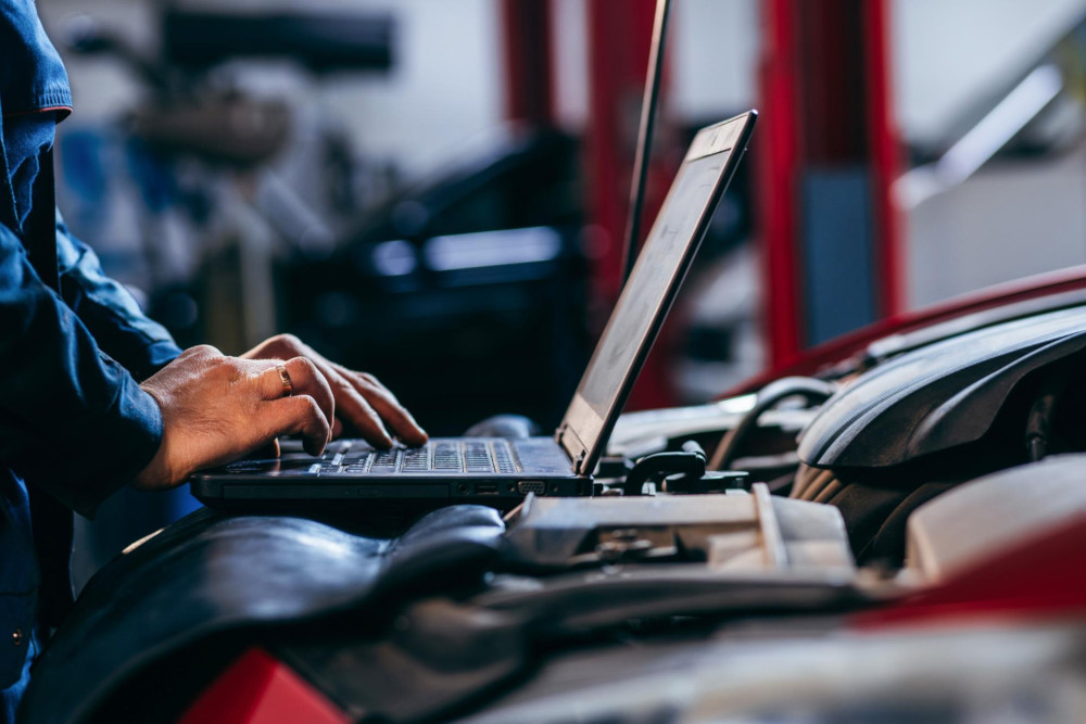 Mechaniker mietet am Laptop über dem Motorraum den passenden Adapter