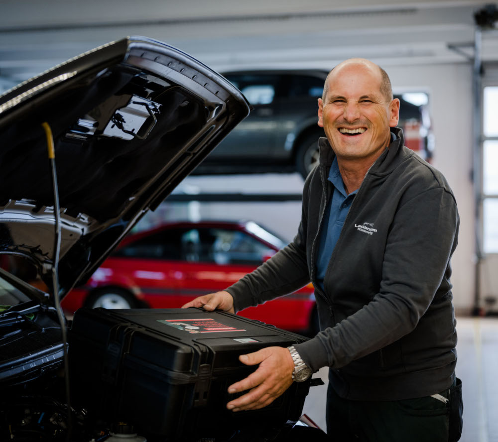 Mechaniker mit mobility-market-Werkzeugkoffer an einem Fahrzeug mit offener Motorhaube